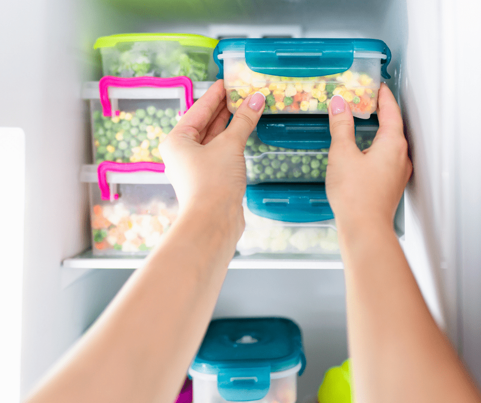 hands stack plastic containers of frozen vegetables in a freezer