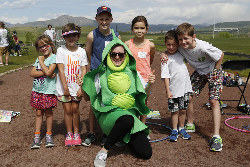 Group of kids huddle around a woman dressed in a snap pea costume