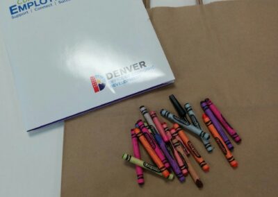 Paper folder that says "colorado employment first, support connect succeed. denver office of economic development over a paper take away bag and a pile of crayons"