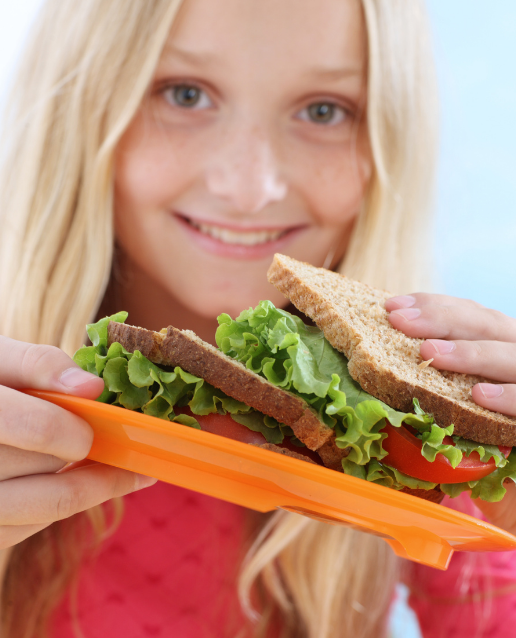 Young teen girl holds a sandwich on an orange plate. She['s smiling at the camera