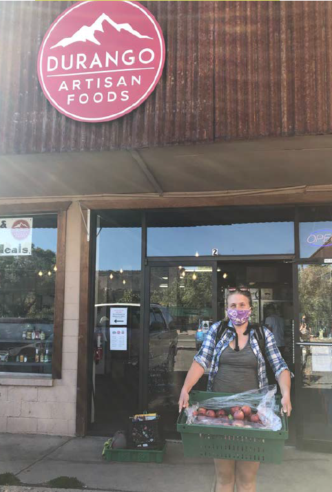 Woman holds a basket of apples in front of a store called Durango Artisan Foods. The Good Food Collective works to build food systems.